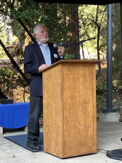 Shelly Zedeck giving a lecture at a wood podium with redwoods behind him